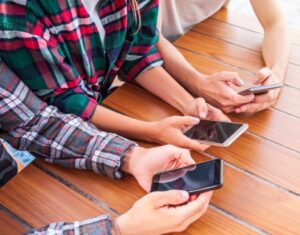 Image shows three people sitting at a wooden table using their smartphones for Google search.